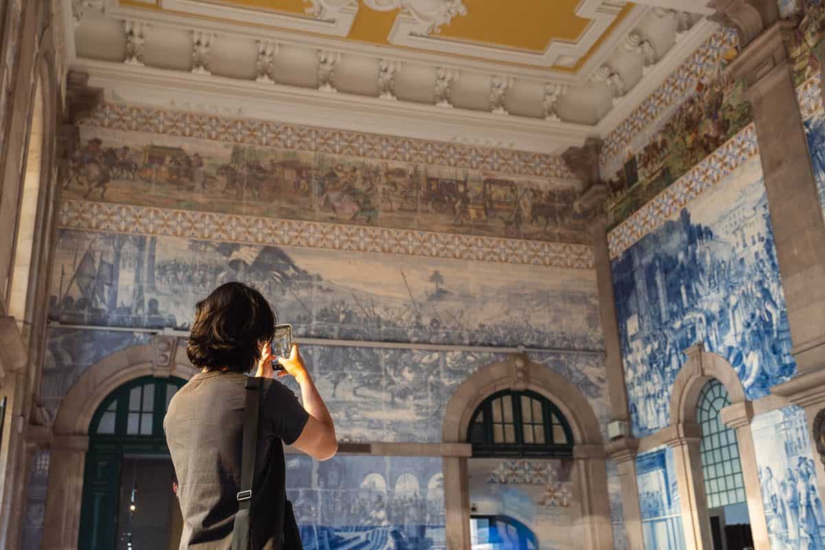 A visitor photographing the azulejo tile murals inside Sao Bento train station