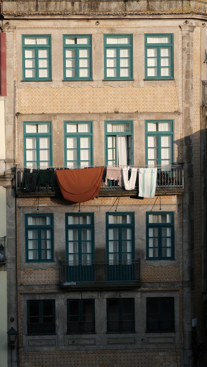 Tiled Porto facade with teal window frames and laundry hanging in evening light